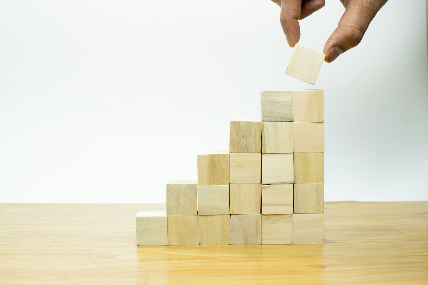 A hand places a wooden block atop a growing stack