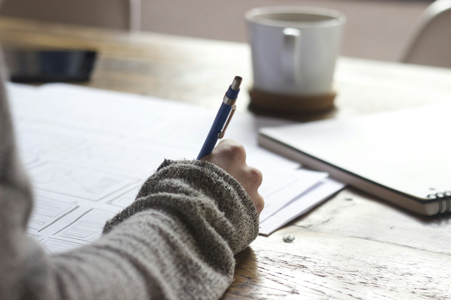 A person sketches ideas at a table with a notebook and coffee